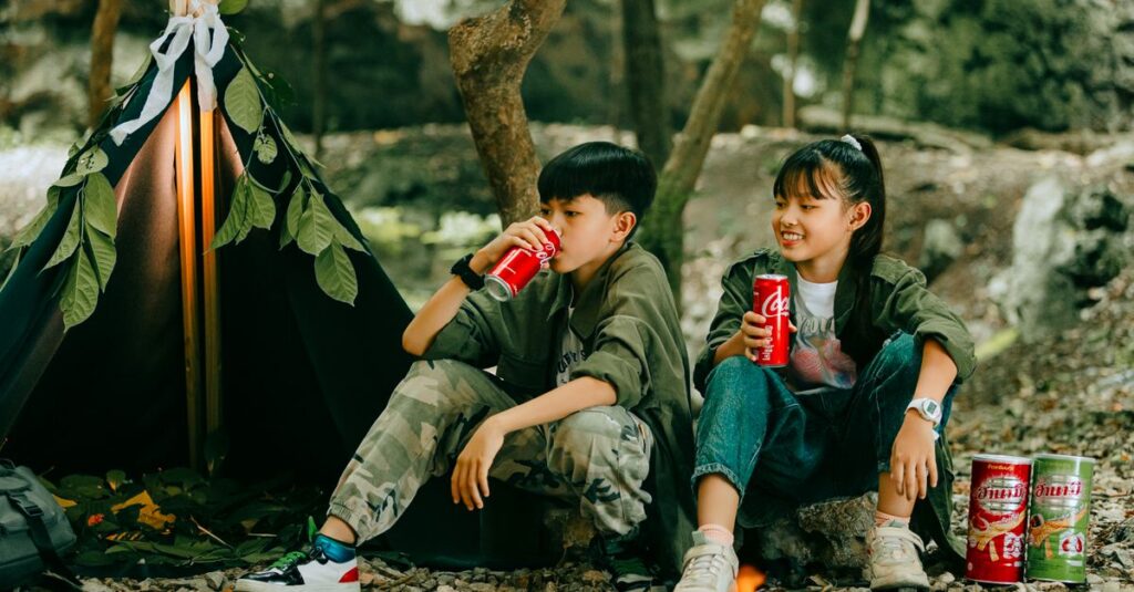 キャンプ場で家族が昼食を囲んで笑顔で過ごす風景。テーブルに並ぶ彩り豊かな料理と子どもたちの楽しそうな表情が印象的。