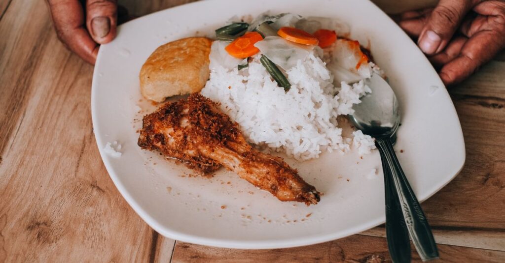 キャンプ場でご飯メニューを食べる子どもたちと両親。焼きおにぎりやカレーチャーハンがテーブルに並ぶ風景。